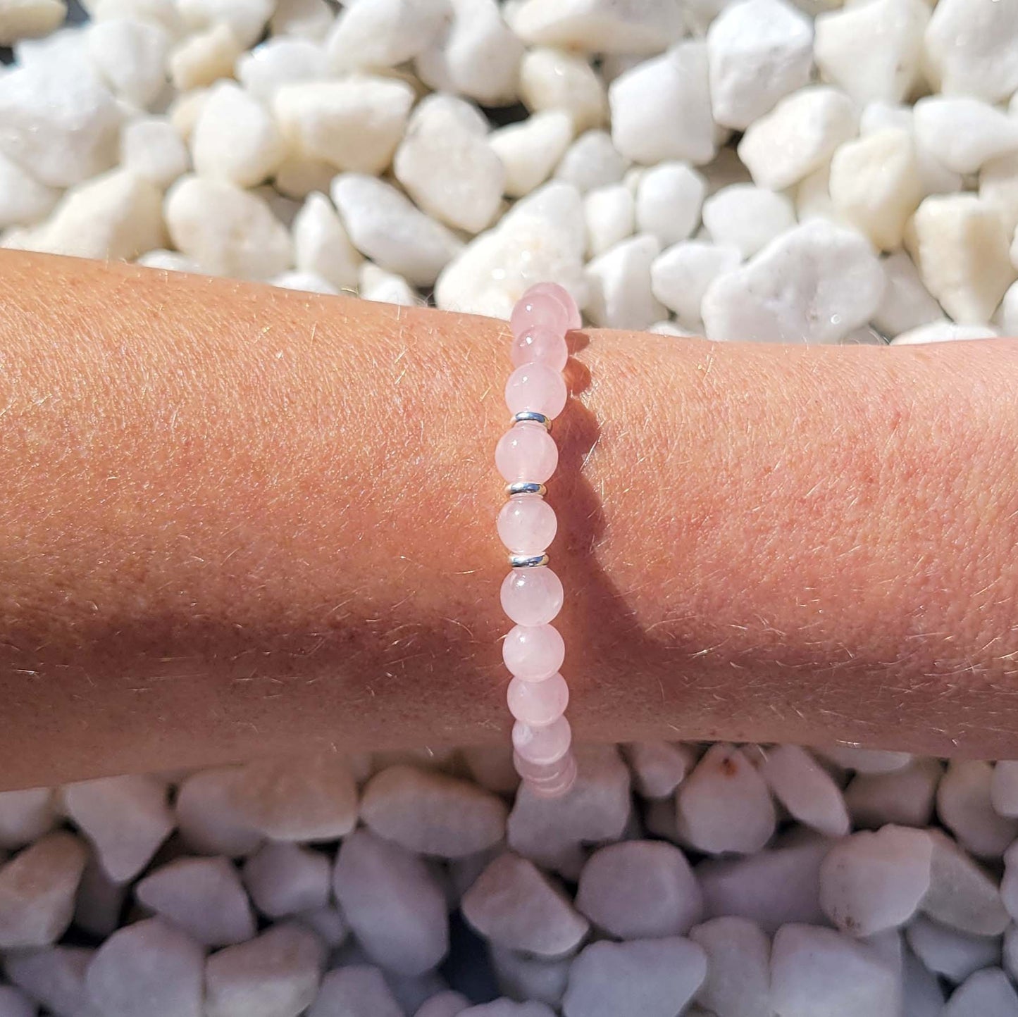 Pink beaded bracelet on a wrist with a background of white pebbles