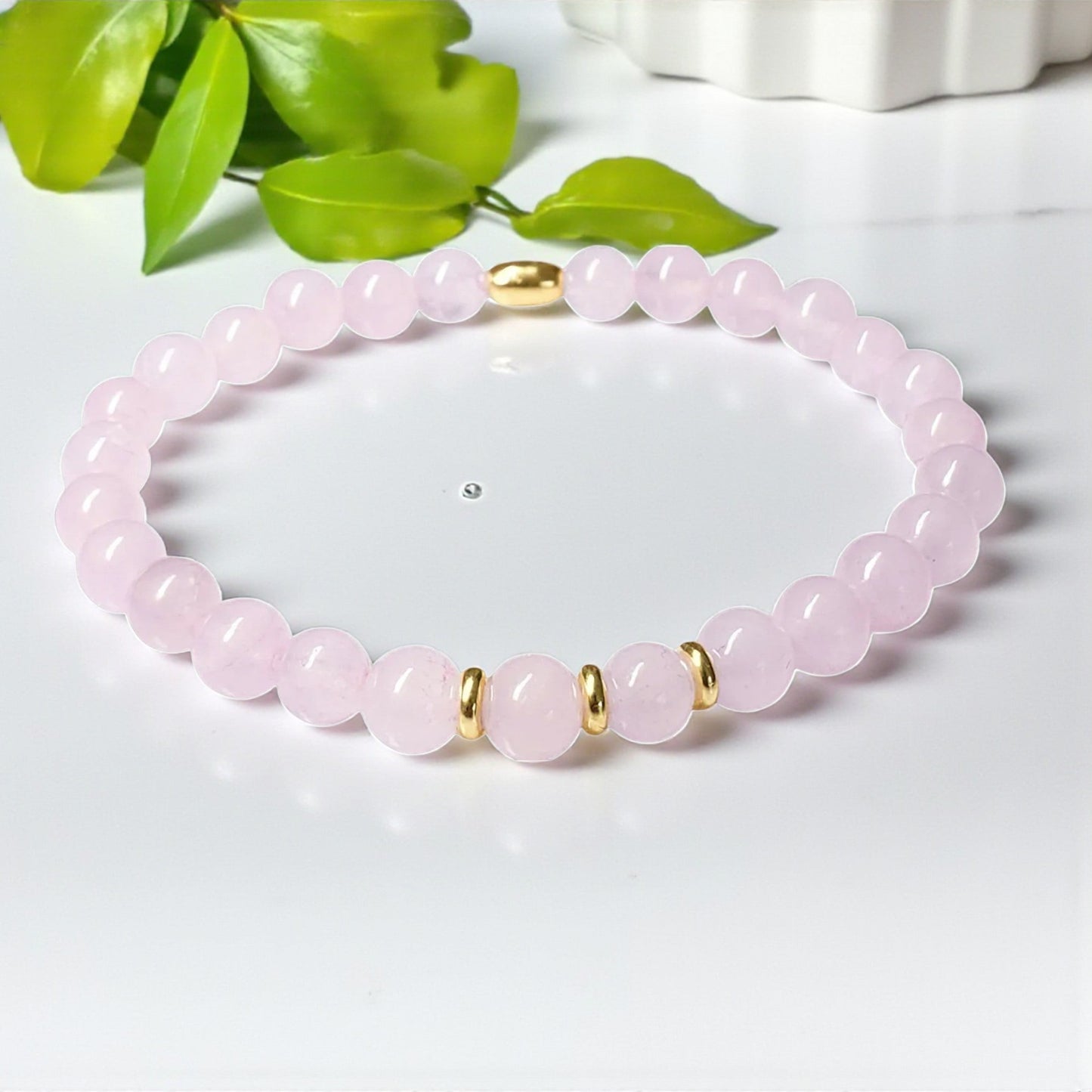 Pink beaded bracelet with gold accents on a white surface with green leaves in the background