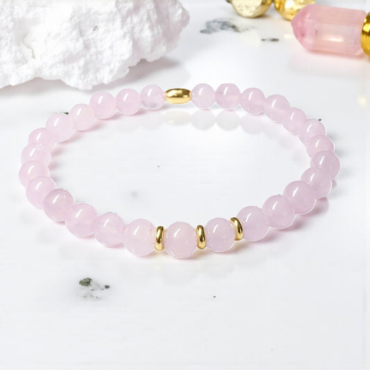 Pink beaded bracelet with gold accents on a white background